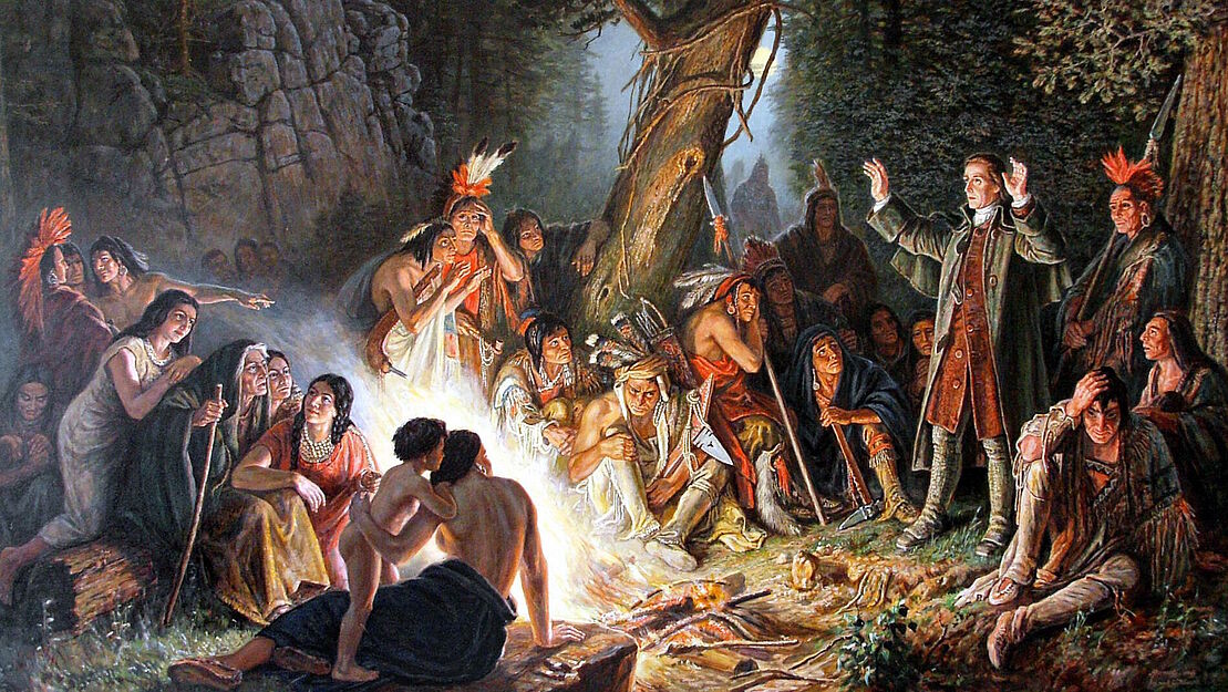 Gemälde von Alfred Bernert nach dem Original von Christian Schussele; zu sehen ist David Zeisberger, wie er vor Indianern am Lagerfeuer steht und predigt